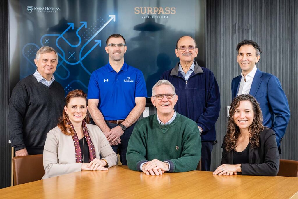 The team working on the BEAST project post together in a conference room. The front row is seated at a wooden table and the back row is standing behind them. Team member names are listed in the text below the image.